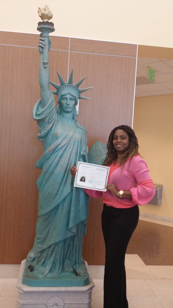 A woman holding her certificate in front of the statue of liberty.